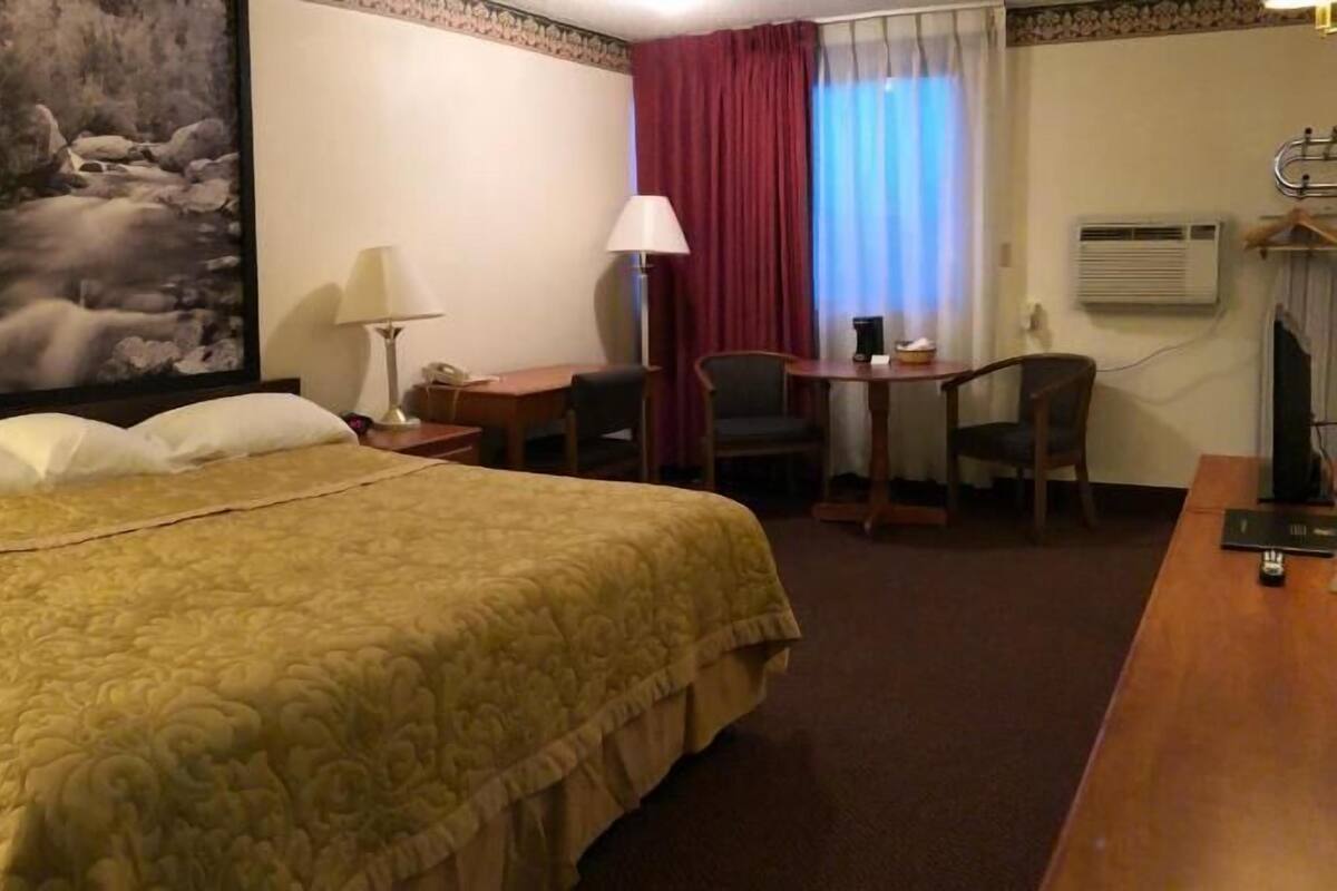 Habitación de hotel con una cama grande, un escritorio, una silla, una lámpara y un cuadro de un río.