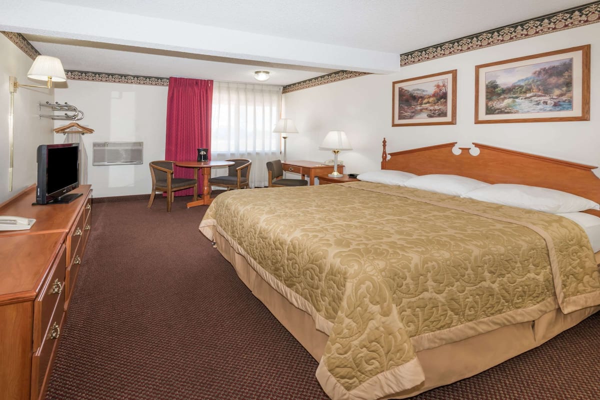 Una habitación de hotel con una cama grande, un escritorio con una silla, un televisor y un aparador.