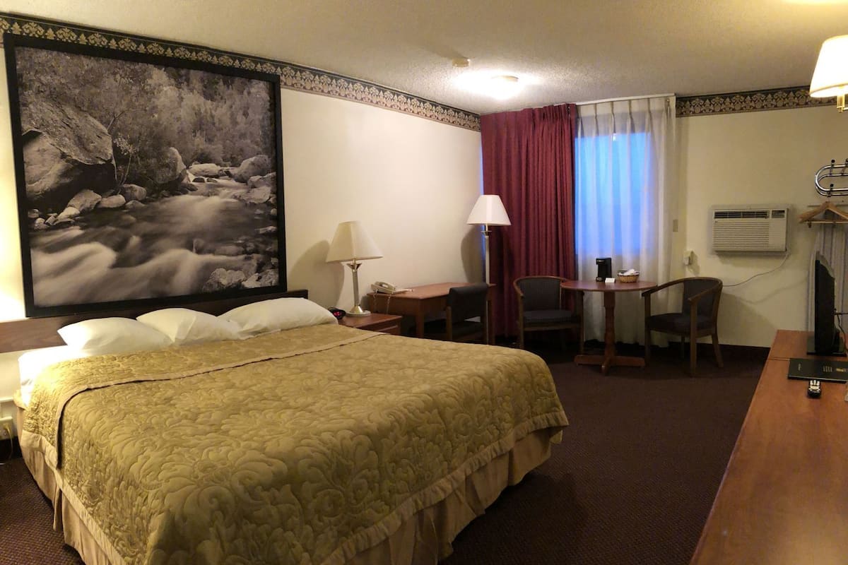 Una habitación de hotel con una cama grande, un escritorio, una silla, una lámpara y un cuadro grande en la pared.