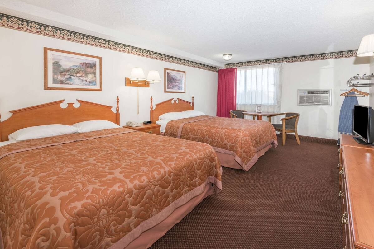 Una habitación de hotel con dos camas, una mesita, una silla, un televisor y un escritorio.