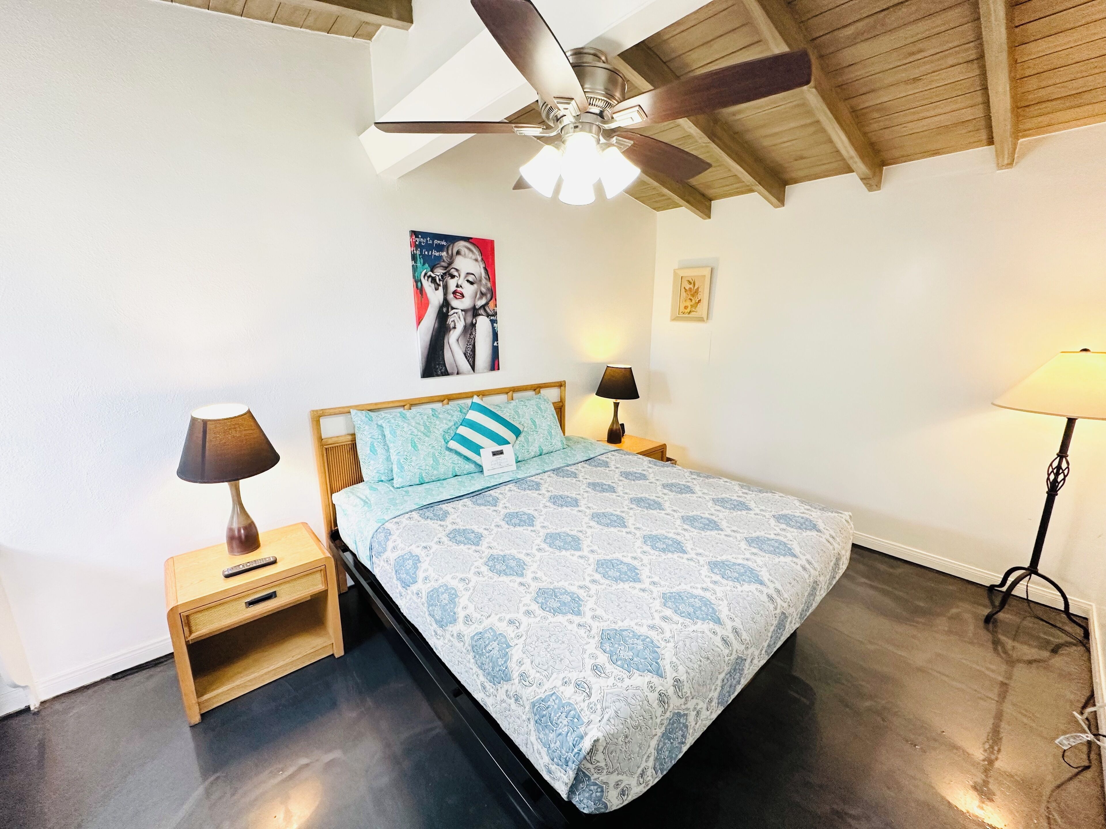 A bedroom with a bed, two bedside tables, a ceiling fan, and a wall-mounted picture.