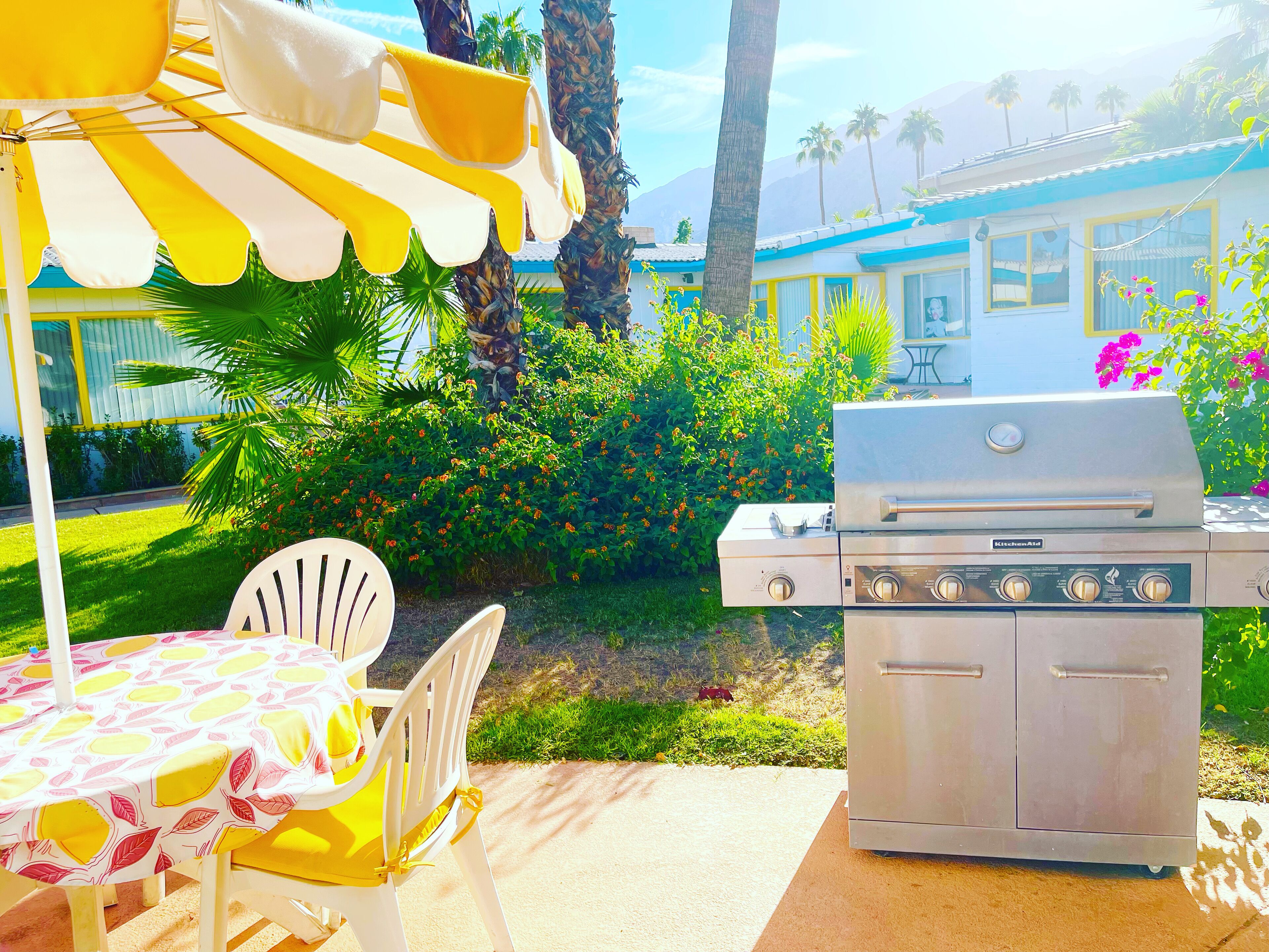 An outdoor patio with a grill, a table with a yellow tablecloth, and a chair.