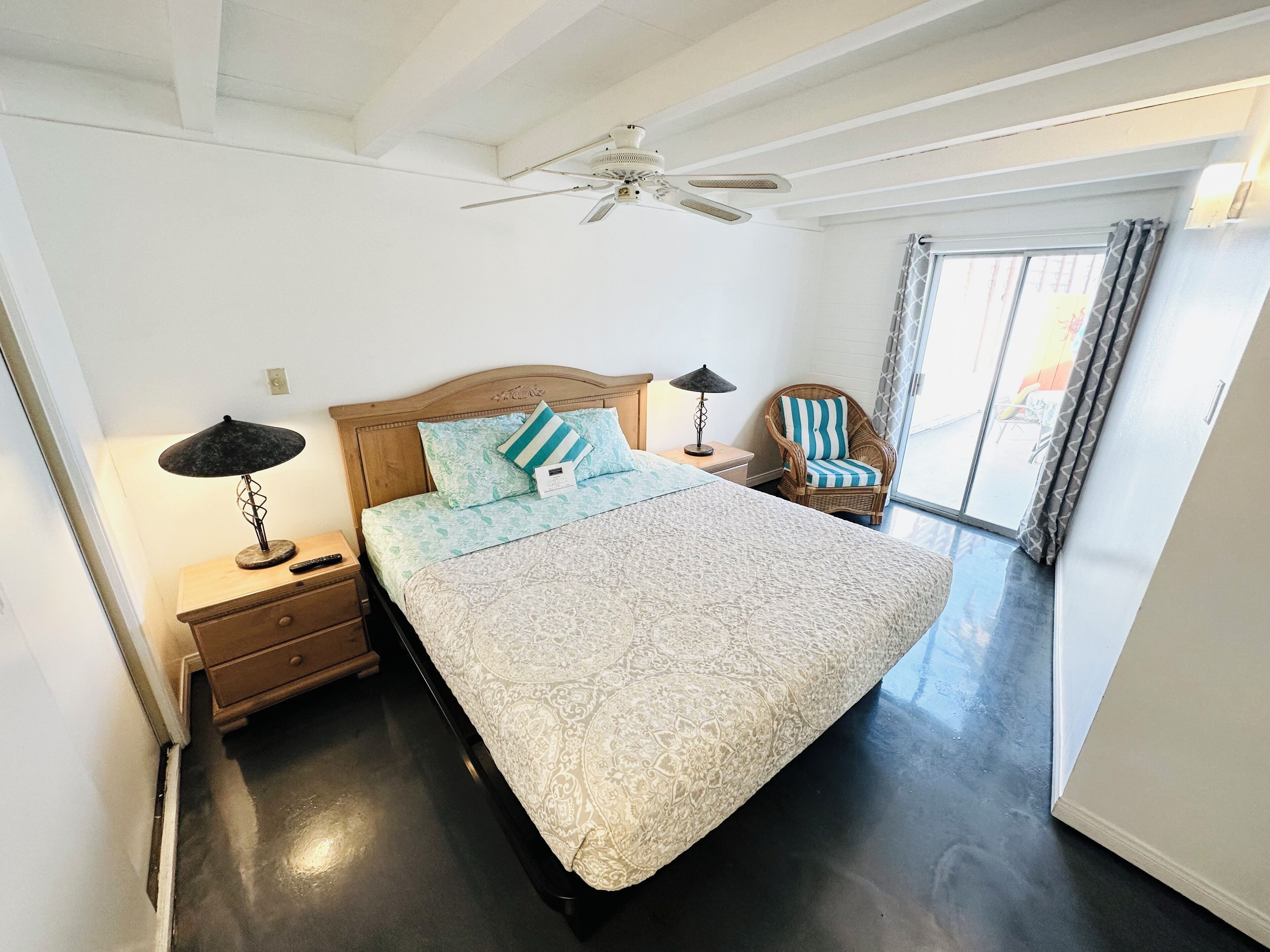 A bedroom with a bed, nightstands, a chair, a ceiling fan, and a view of the outdoors.