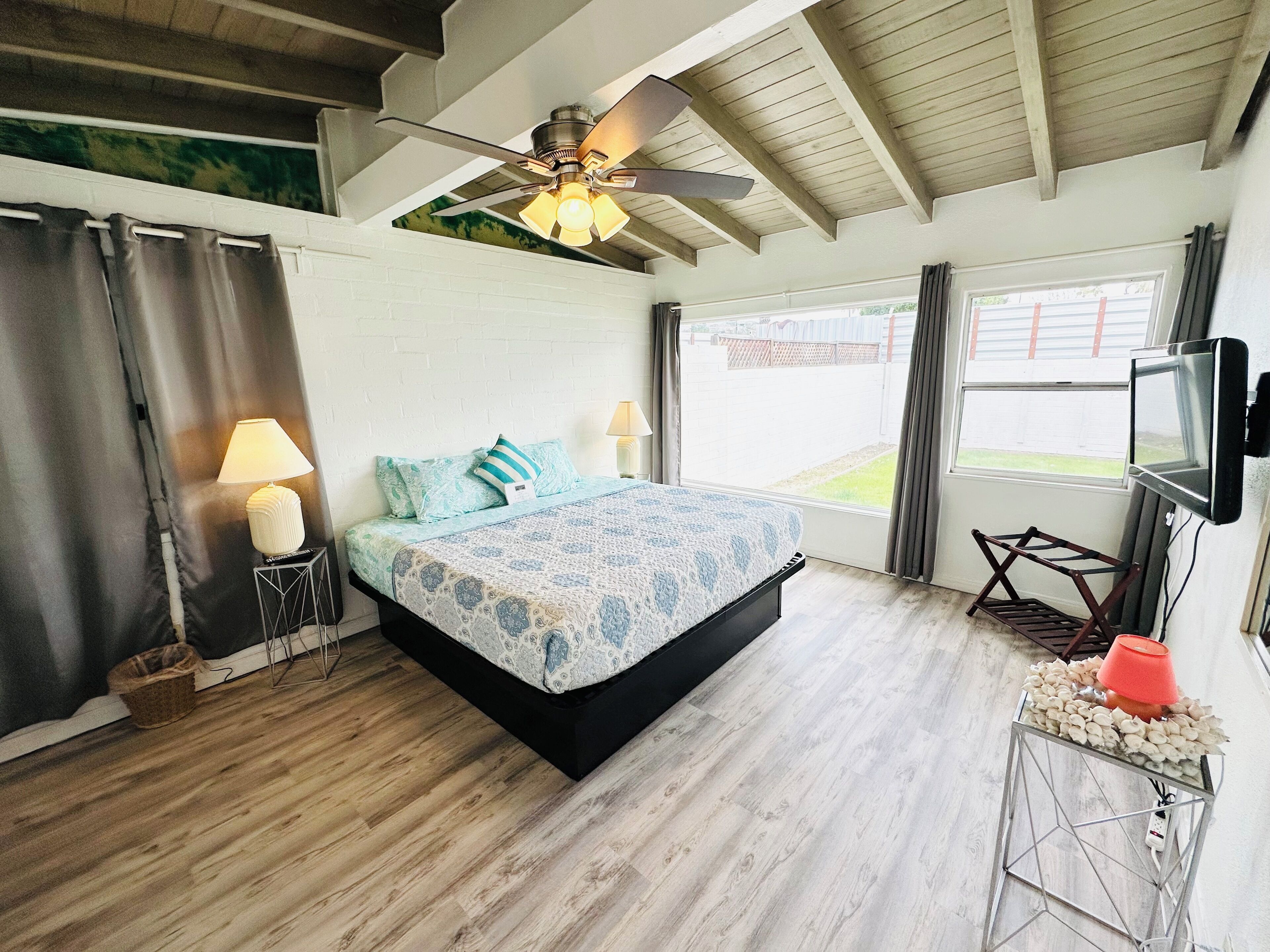 A bedroom with a bed, a ceiling fan, a TV, and a window.