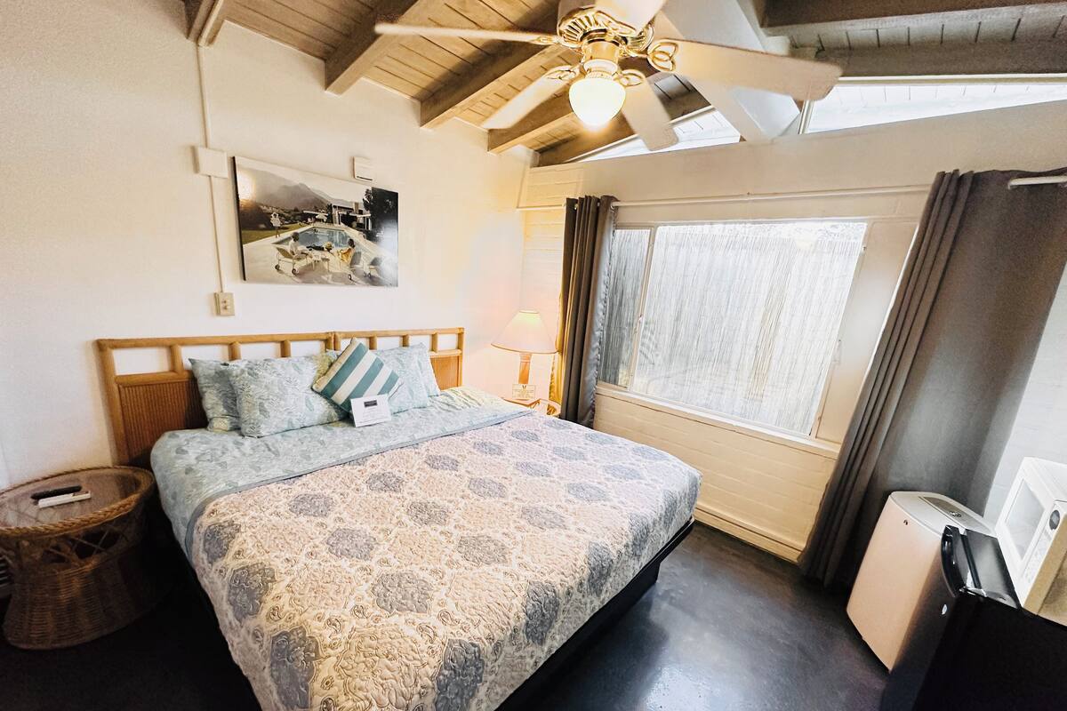 A bedroom with a bed, a ceiling fan, a window with curtains, and a small table.