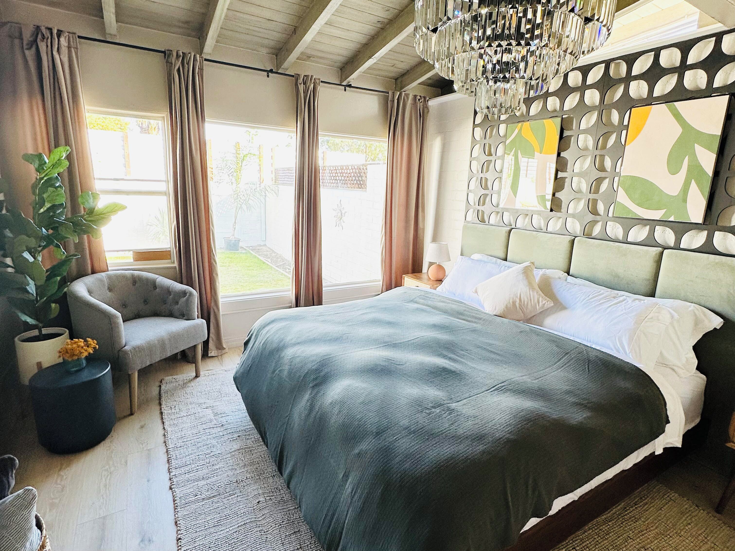 A bedroom with a large bed, a chair, a potted plant, and a chandelier.