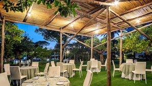An outdoor dining area with tables set for a meal, surrounded by chairs and a bamboo pergola structure. - Hotel Alpha (Sant'Agnello)