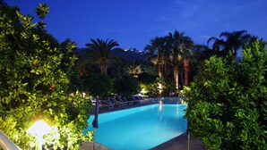A swimming pool surrounded by palm trees and lounge chairs, with a stone pathway leading to the pool. - Hotel Alpha (Sant'Agnello)