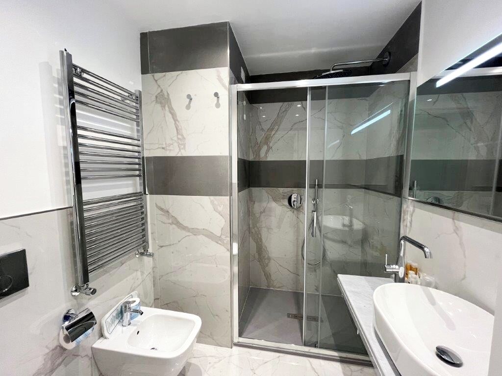 A modern bathroom with a glass-enclosed shower, two sinks, and a towel rack.