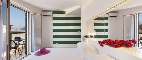 A modern hotel room with a large bed, a balcony with a table, and a green-striped wall.