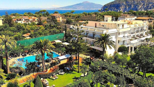 A resort with a swimming pool, lush greenery, and a mountain in the background. - Hotel Alpha (Sant'Agnello)