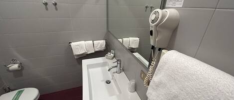 Un baño con un lavamanos blanco, un espejo, un secador de pelo y dos toallas colgadas de ganchos.