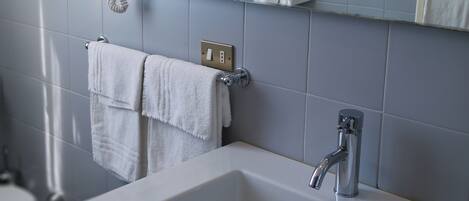 Un baño con lavamanos blanco, espejo y toallero.