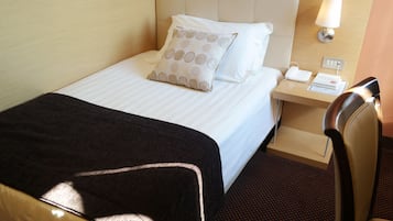 A hotel room with a bed, a nightstand with a lamp, a phone, and a chair.