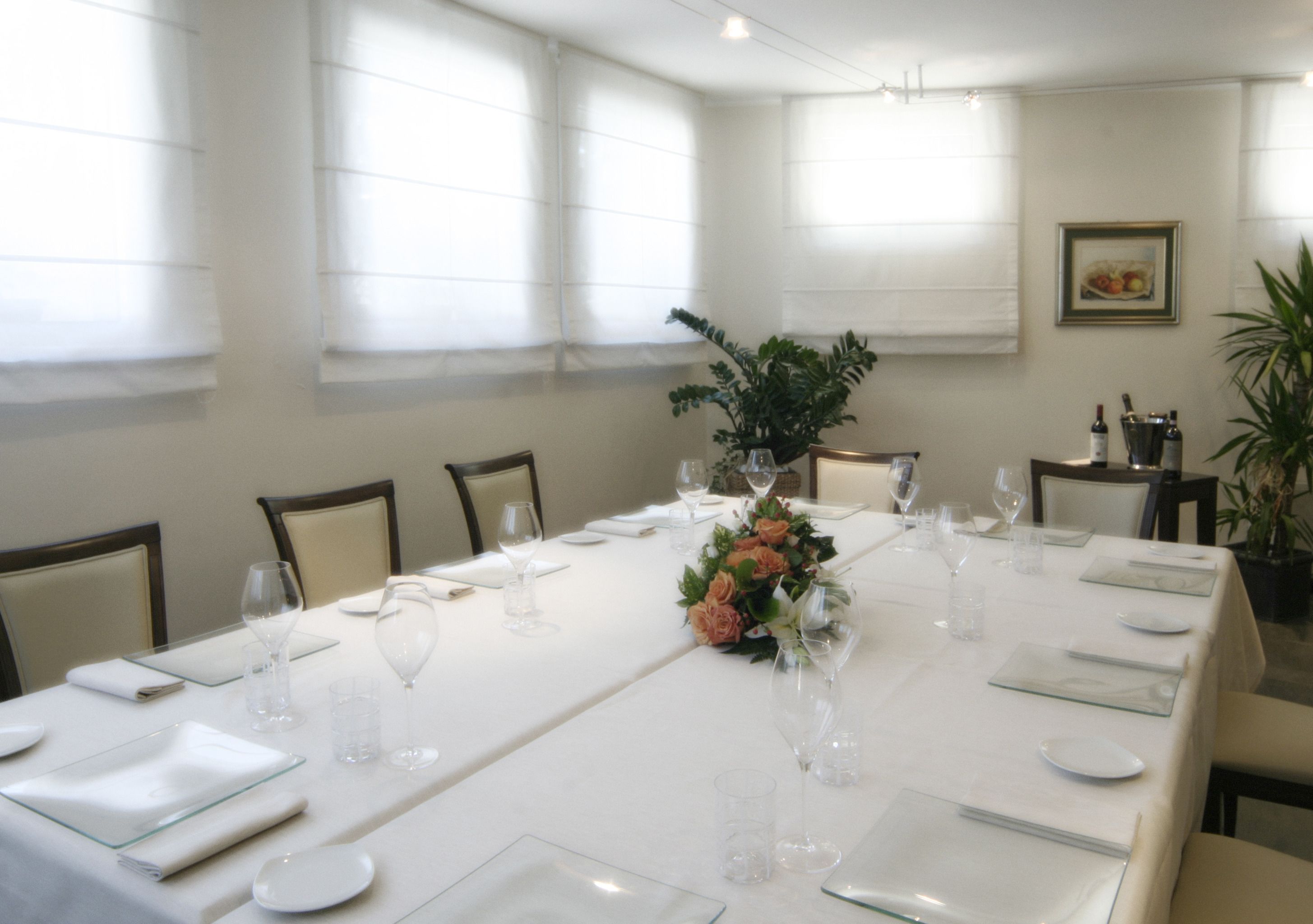 Un salón de conferencias con una larga mesa dispuesta para una reunión, equipado con sillas, vasos y una decoración floral.