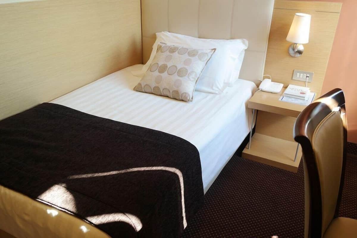 Una habitación de hotel con una cama, una mesita de noche con lámpara, un teléfono y una silla.