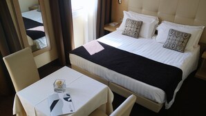 A hotel room with a bed, a table with a chair, a nightstand, and a mirror. - Vittoria Hotel (Rubano)