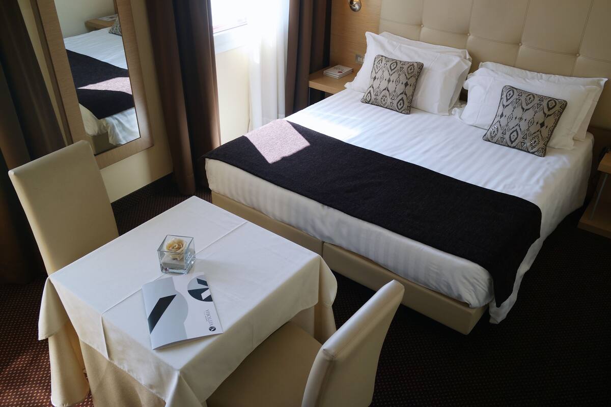 Una habitación de hotel con cama, una mesa con silla, mesita de noche y espejo.