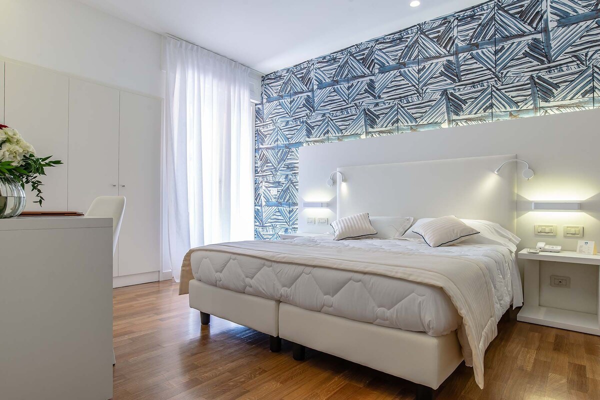 Une chambre moderne avec un grand lit, des murs blancs et un papier peint à motifs.