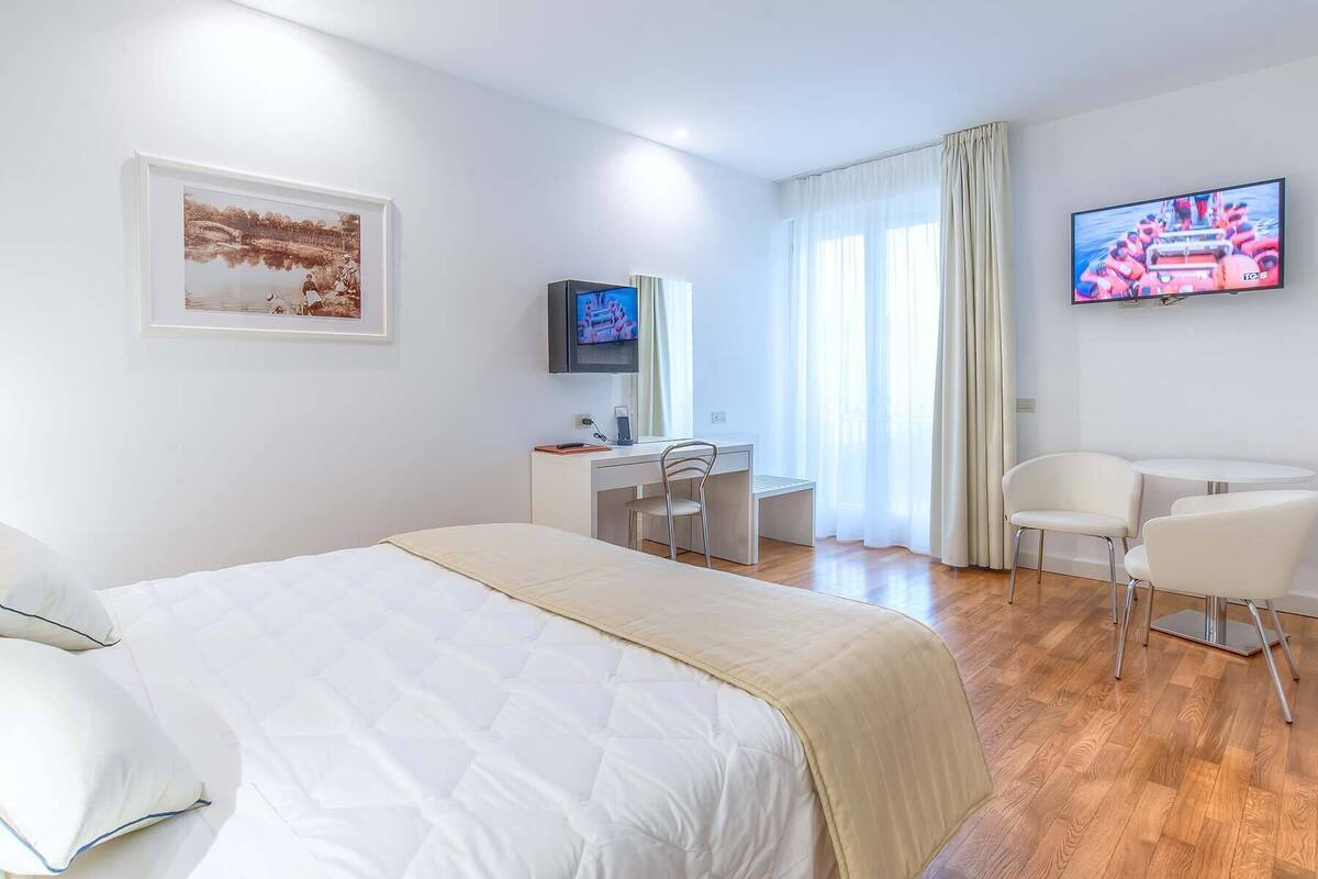 A hotel room with a bed, a desk, a chair, a TV, and a window with curtains.