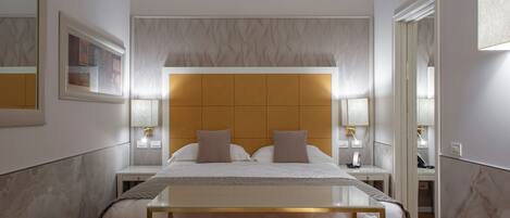 A modern hotel room with a large bed, bedside lamps, a nightstand, and a mirror.