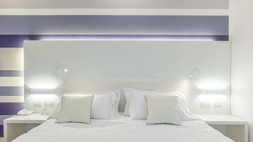 Een netjes opgemaakt bed met witte lakens en kussens, aan weerszijden met nachtkastjes, lampen en een telefoon.