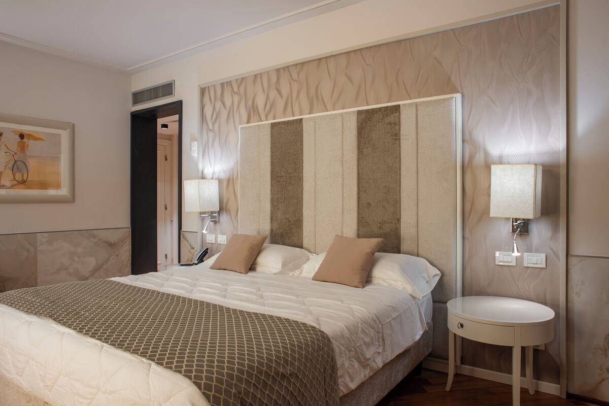 A hotel room with a large bed, a bedside table with a lamp, and a wall-mounted light fixture.