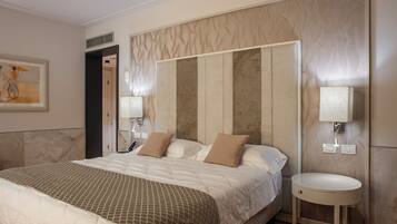 A hotel room with a large bed, a bedside table with a lamp, and a wall-mounted light fixture.