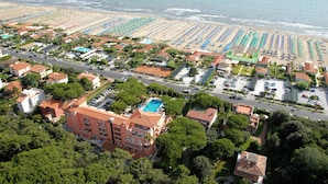 An aerial view of a coastal resort with multiple buildings, a large beach area with rows of umbrellas, and a swimming pool. - Versilia Palace Hotel (Pietrasanta)