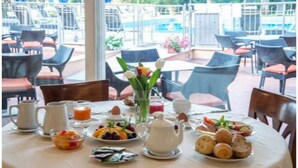 A breakfast table set with various fruits, pastries, and beverages, surrounded by chairs and a view of a pool and garden. - Versilia Palace Hotel (Pietrasanta)