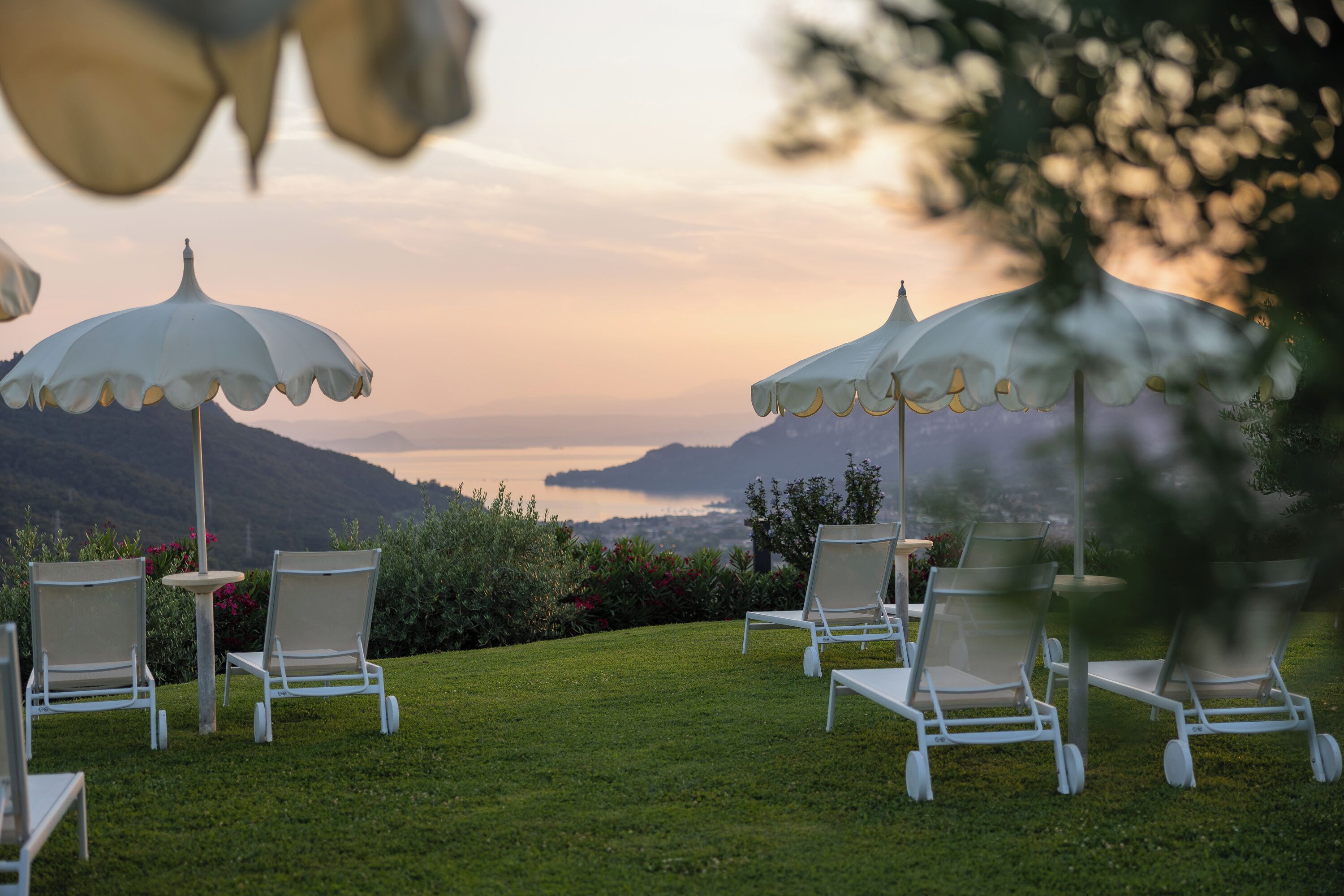 A serene outdoor seating area with white chairs and umbrellas, overlooking a scenic landscape with hills and a body of water.