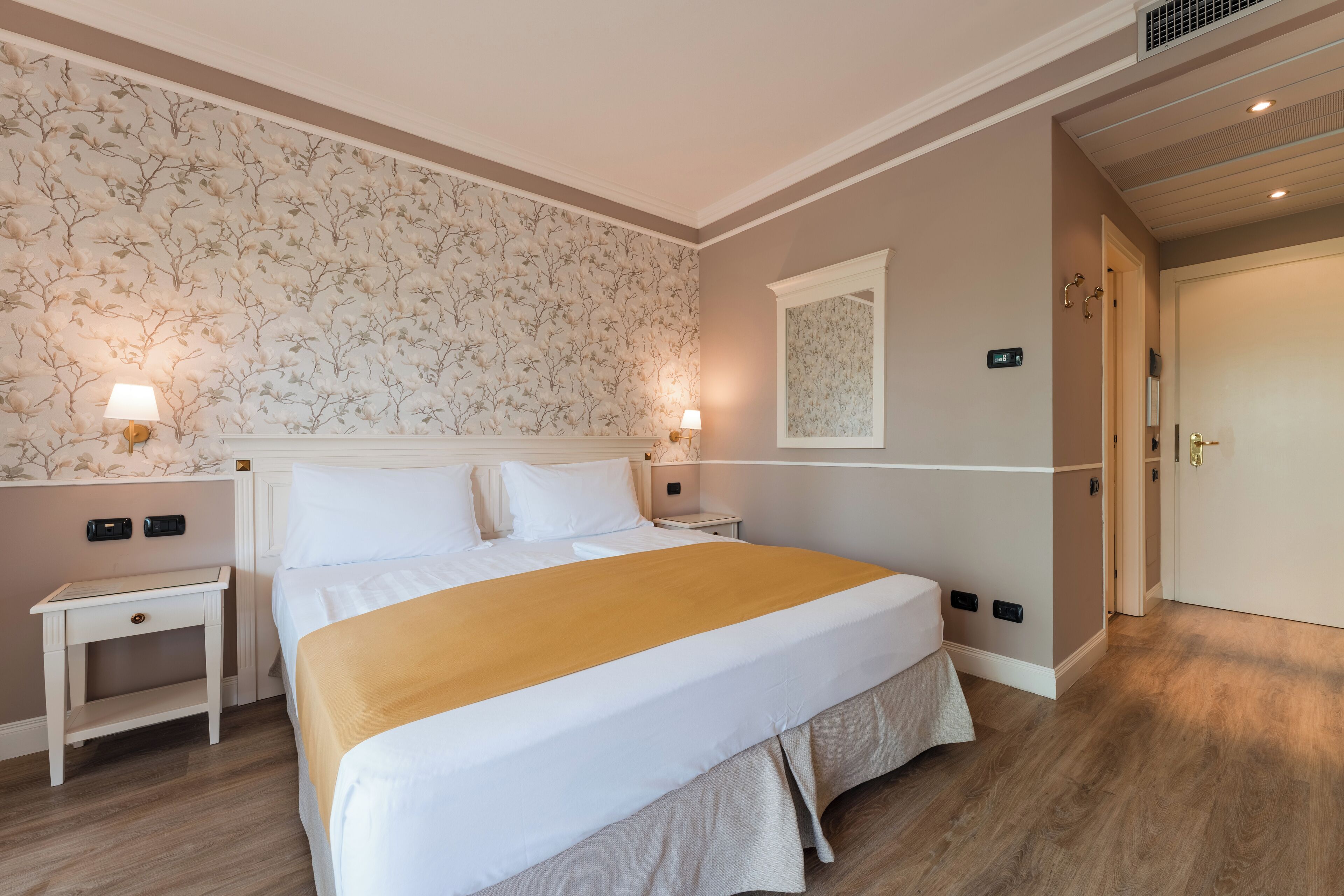 A neatly arranged bedroom with a large bed, bedside tables, a nightstand, and a mirror.