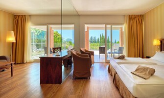 Habitación de hotel con piso de madera, cama con colcha color beige, escritorio con silla y balcón con sillas.