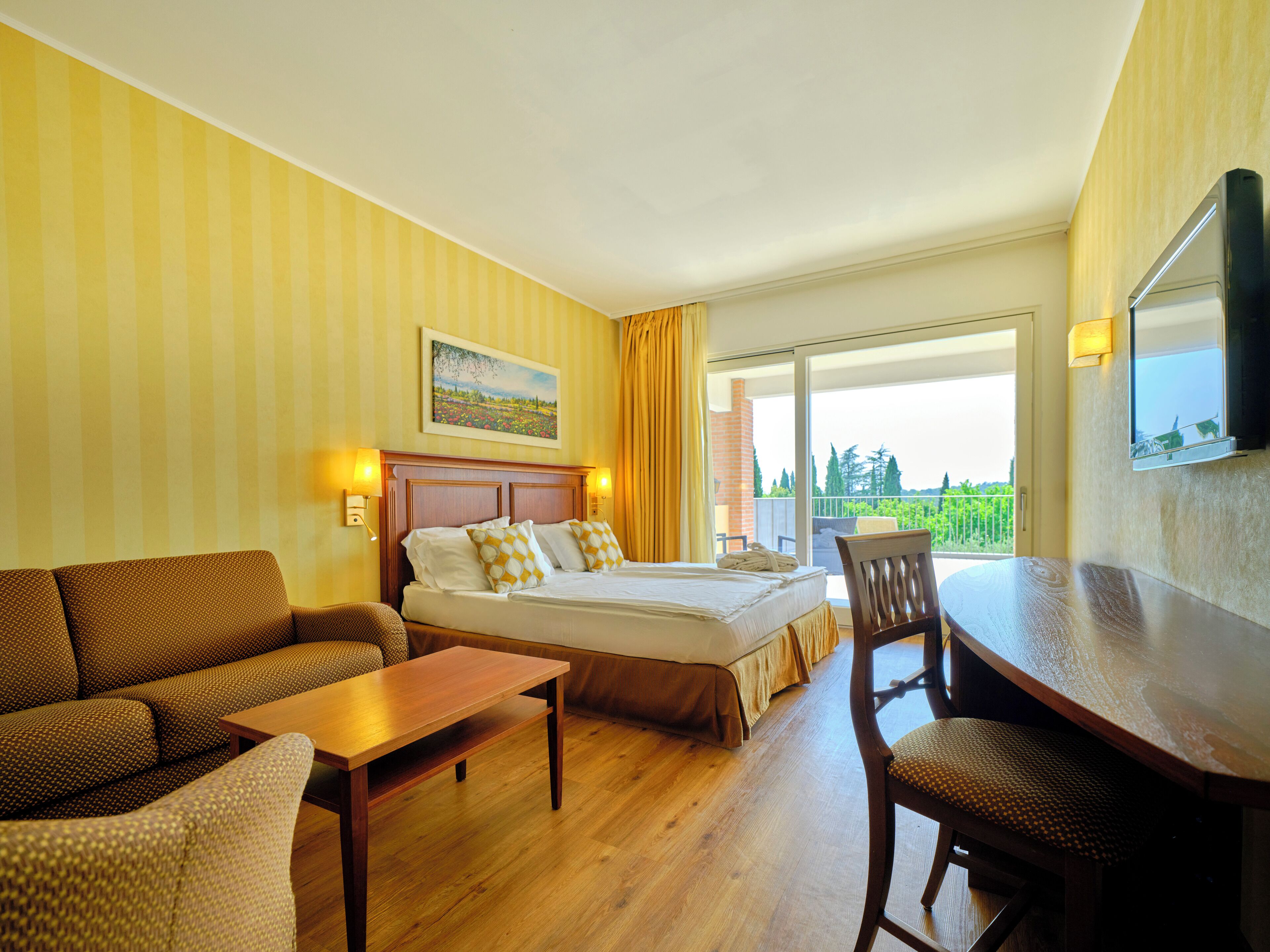 A hotel room with a bed, a sofa, a desk, and a balcony with a view.