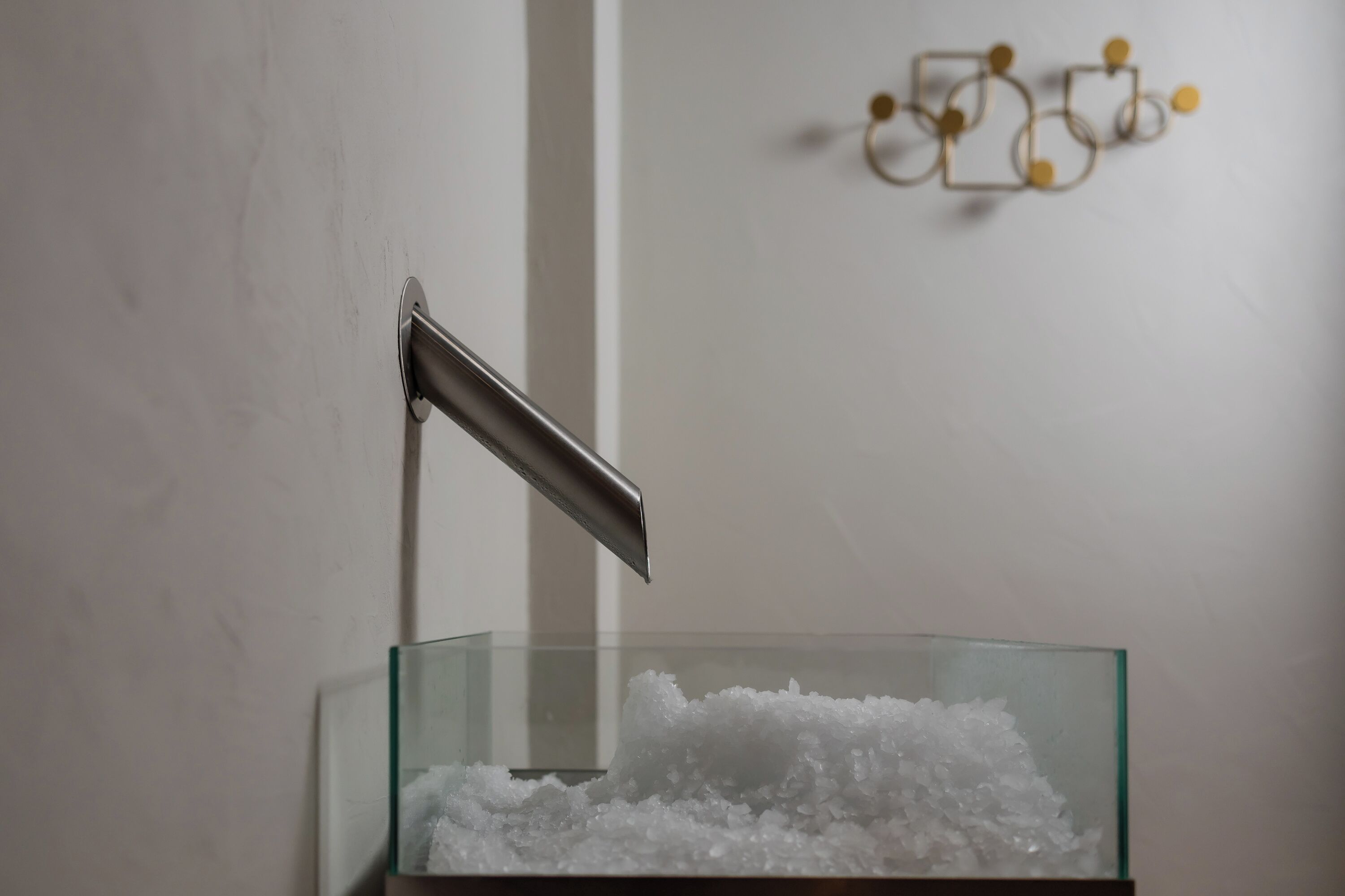 A bathroom with a glass container filled with white bath salts, a metal towel rack, and a wall-mounted decorative object.