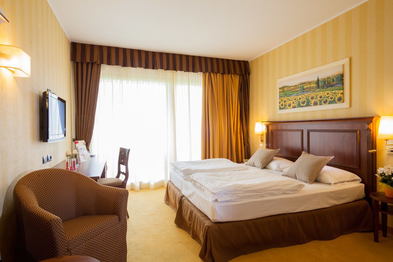 Een hotelkamer met een groot bed, een stoel, een bureau en een schilderij aan de muur.