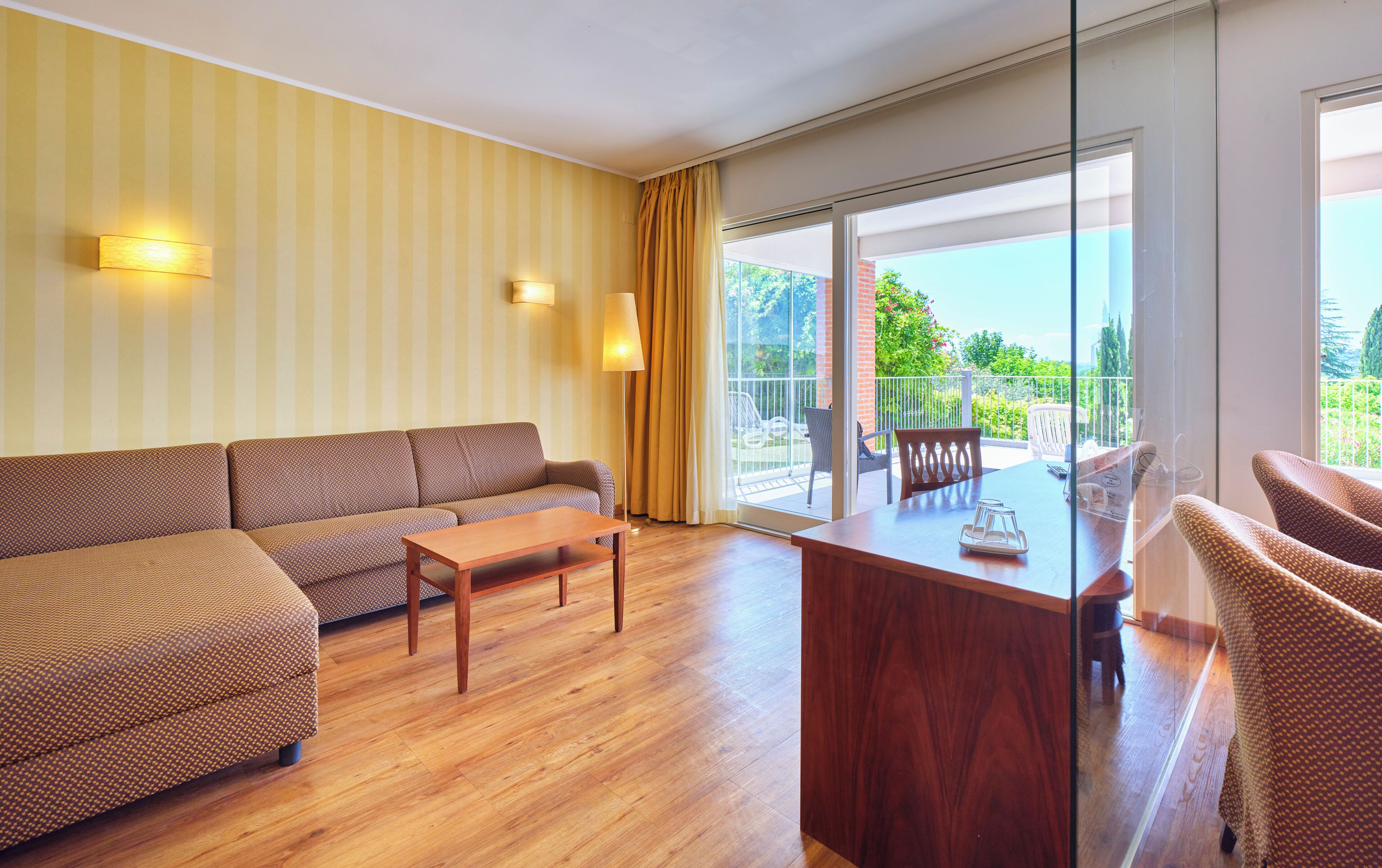 A modern living room with a sofa, a wooden coffee table, and a balcony with a view of greenery.