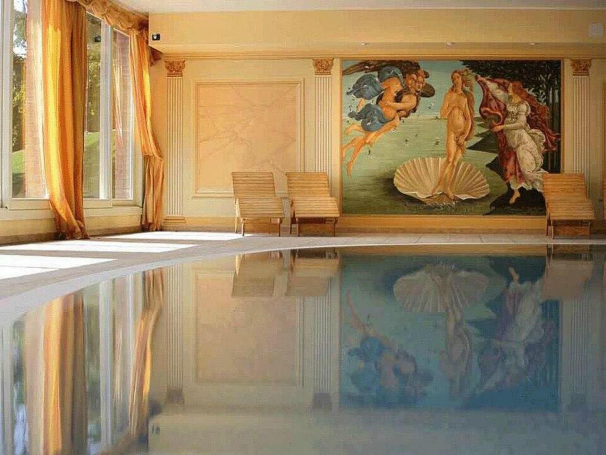 Une pièce dotée d’une grande piscine, d’une fresque représentant des figures classiques et d’un espace détente avec des fauteuils.