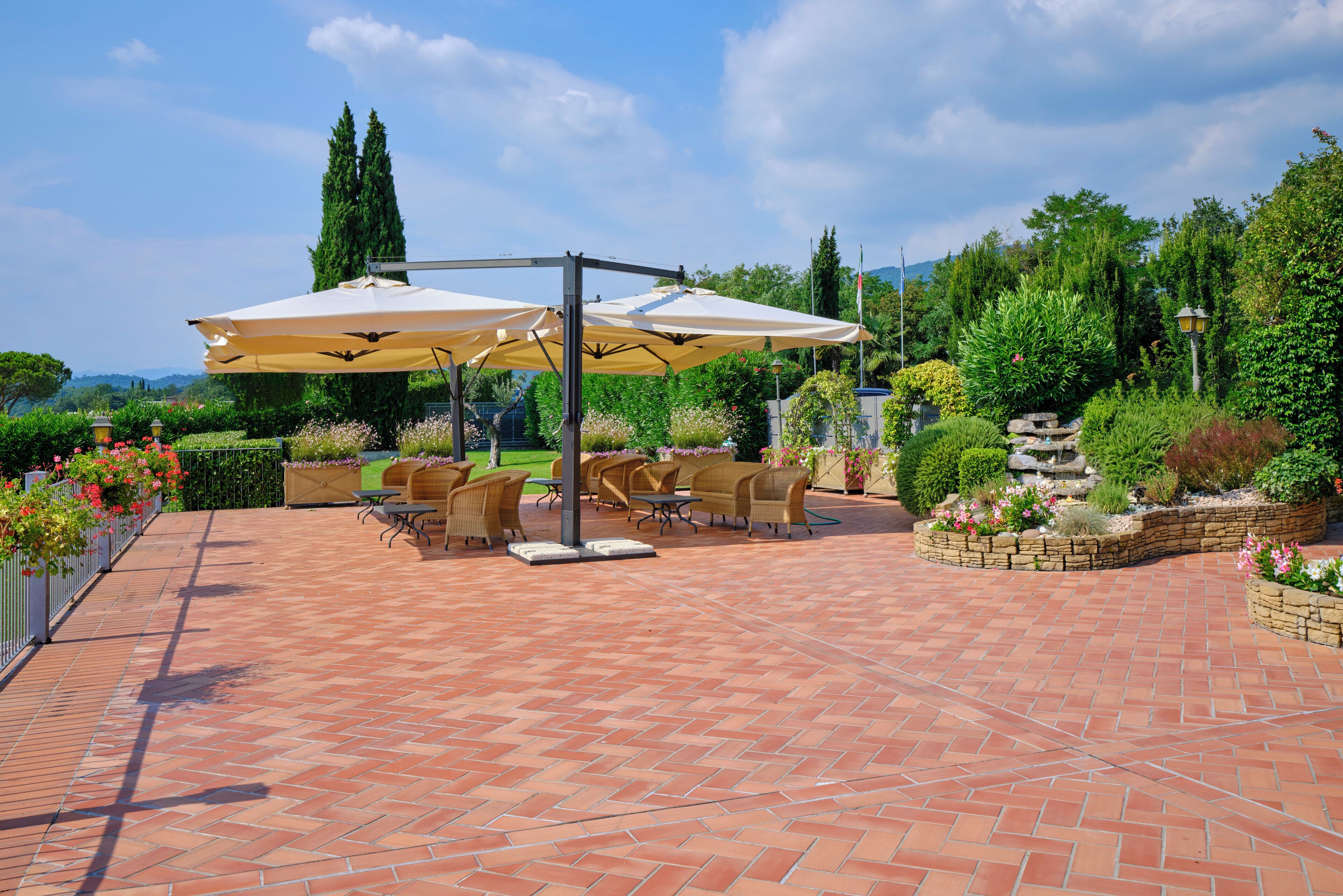 A patio area with outdoor furniture and umbrellas, surrounded by lush greenery and a stone pathway.