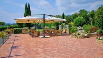 A patio area with outdoor furniture and umbrellas, surrounded by lush greenery and a stone pathway.