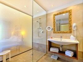 Un baño moderno con cabina de ducha de vidrio, tocador con lavabo y espejo con marco dorado.