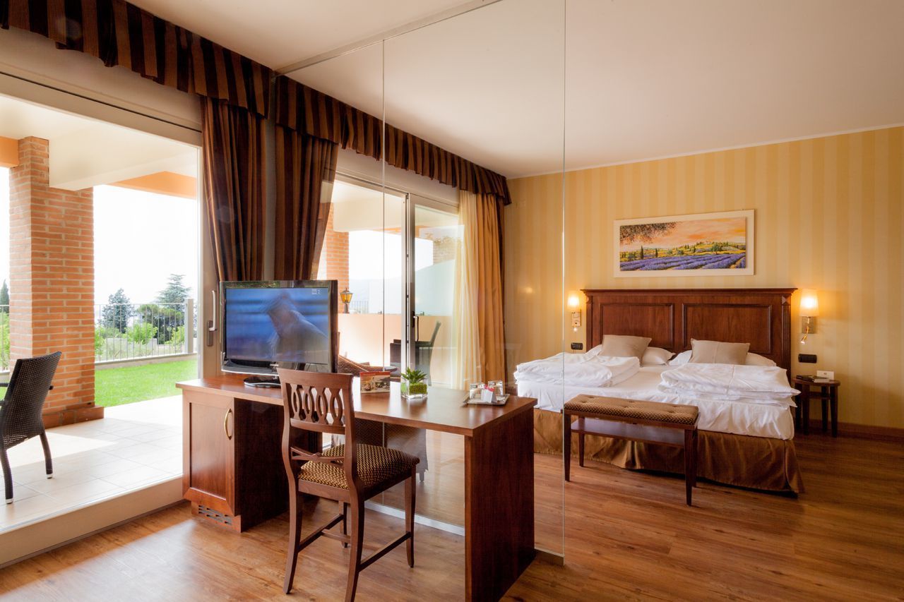 A hotel room with a bed, a desk with a chair, a television, and a painting on the wall.