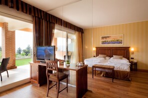 A hotel room with a bed, a desk with a chair, a television, and a painting on the wall. - Hotel Boffenigo  The Golden Hour (Costermano sul Garda)