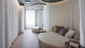 Una habitación de hotel moderna con un sofá curvo, una mesa de centro redonda y una mesita auxiliar.