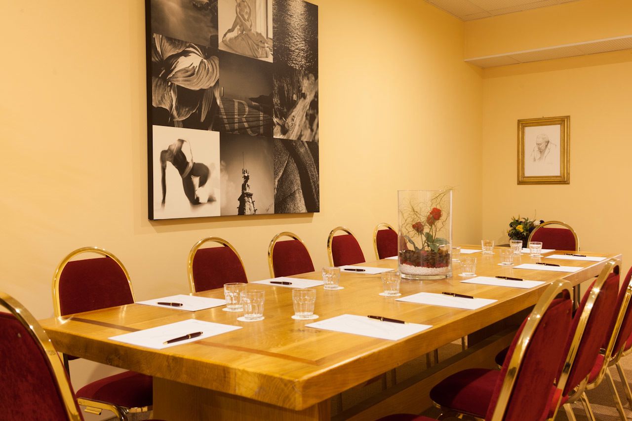 A conference room with a long table, red chairs, and a large abstract art piece on the wall.