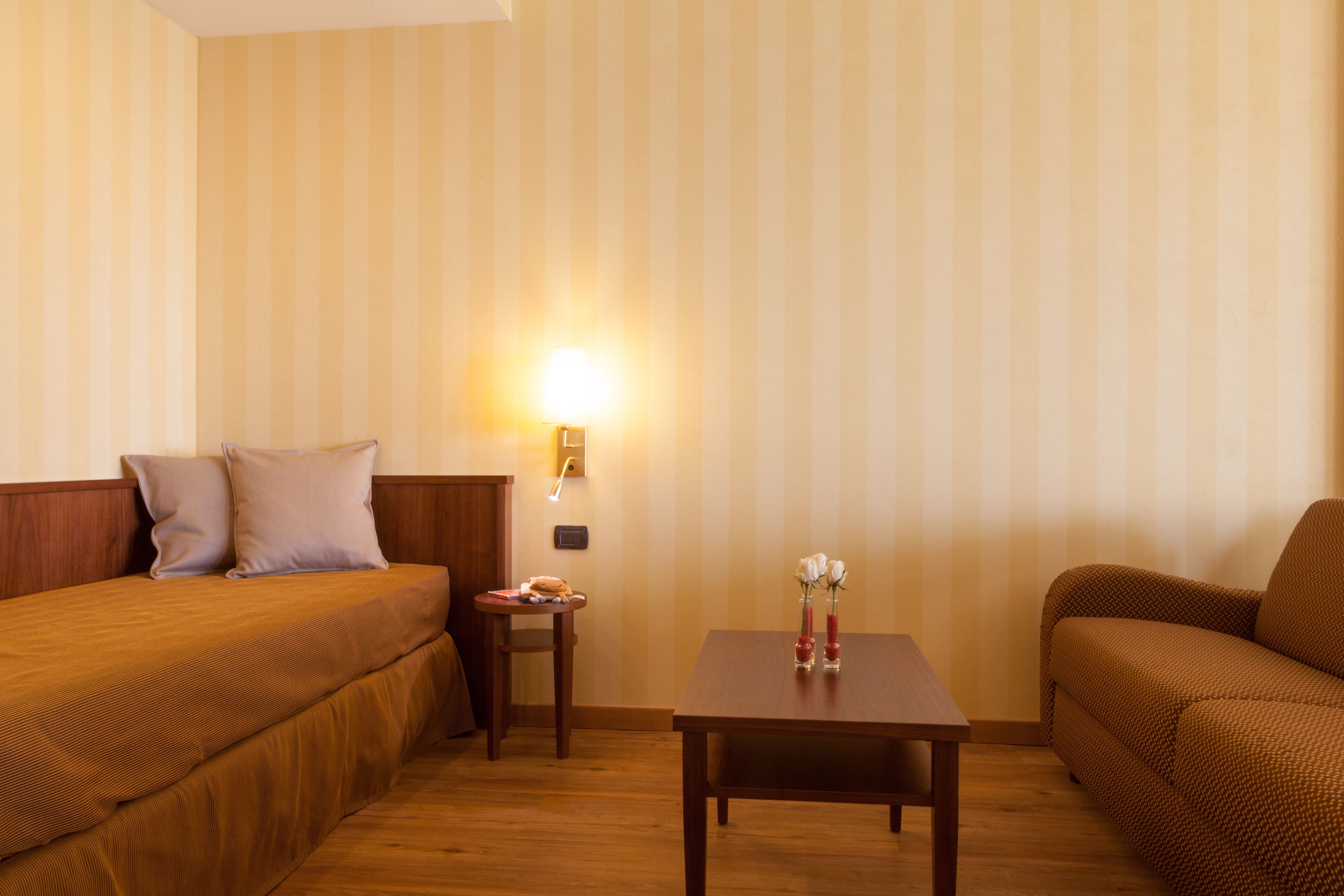 A hotel room with a wooden bed, a small table with a lamp, and a sofa.