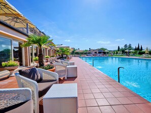 Zona junto a la piscina con sillones de descanso, un suelo de baldosas y una piscina azul cristalina.