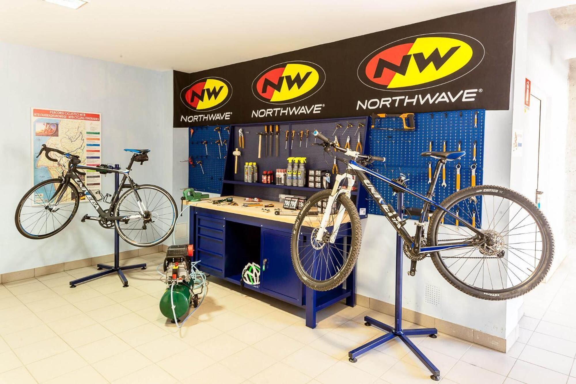 A bicycle repair shop with two bicycles on stands, a workbench with tools, and a wall-mounted pegboard with tools.