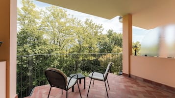 Un balcón con dos sillas y una mesa, rodeado por una barandilla de metal, con vistas a un jardín con árboles.