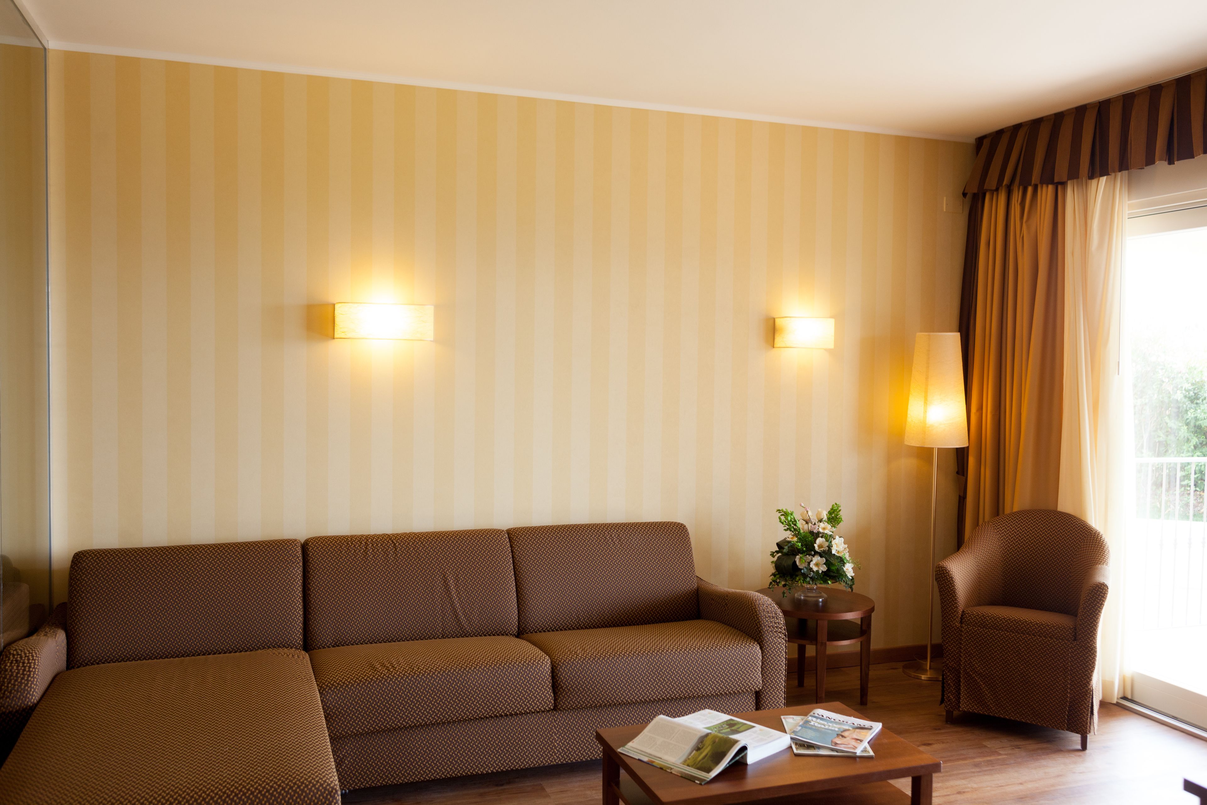 A living room with a brown sofa, a small table with magazines, a chair, and a lamp.
